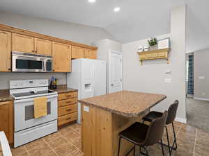 Kitchen with a breakfast bar, white appliances, recessed lighting, lofted ceiling, and a kitchen island