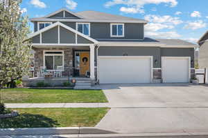 Craftsman inspired home featuring stone siding, stucco siding, a front yard, covered porch, and driveway