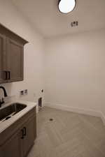 Clothes washing area featuring visible vents, baseboards, hookup for a washing machine, electric dryer hookup, and a sink