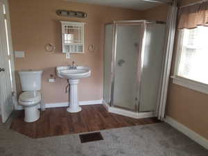 Full bathroom featuring toilet, baseboards, wood finished floors, visible vents, and a stall shower