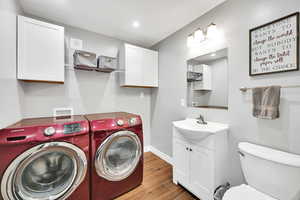 Bathroom with visible vents, vanity, wood finished floors, washing machine and dryer, and toilet