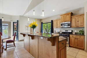 Kitchen featuring appliances with stainless steel finishes, a breakfast bar, dark stone countertops, and light tile patterned flooring