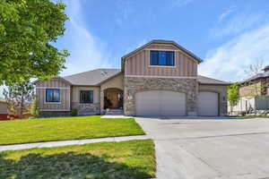 View of front of home with a garage, a front lawn, stone siding, board and batten siding, and driveway
