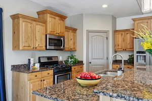 Kitchen featuring appliances with stainless steel finishes, a sink, dark stone countertops, recessed lighting, and an island with sink