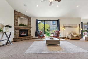 Carpeted living area featuring a stone fireplace, a ceiling fan, recessed lighting, and vaulted ceiling
