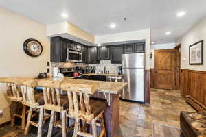 Kitchen featuring tasteful backsplash, stainless steel appliances, stone tile floors, a peninsula, and a kitchen breakfast bar