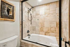 Full bathroom with toilet, a combined bath / shower with jetted tub, and a textured wall
