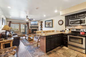 Kitchen with light stone counters, appliances with stainless steel finishes, ceiling fan, a peninsula, and a kitchen breakfast bar