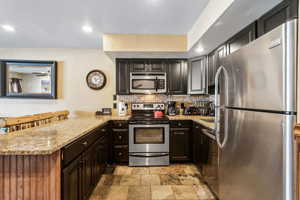 Kitchen with light stone countertops, backsplash, a peninsula, stone finish floor, and appliances with stainless steel finishes