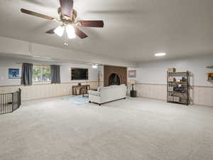 Carpeted living area featuring a wainscoted wall, ceiling fan, a brick fireplace, and a textured ceiling
