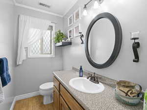 Bathroom with visible vents, ornamental molding, vanity, wood finished floors, and toilet