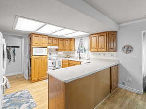 Kitchen featuring light wood-style floors, white appliances, light countertops, a peninsula, and decorative backsplash