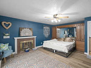 Bedroom featuring wood finished floors, a fireplace, baseboards, a textured ceiling, and a ceiling fan