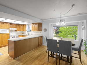 Kitchen featuring white appliances, light countertops, a textured ceiling, under cabinet range hood, and light wood-style flooring