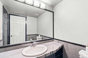 Bathroom featuring tile walls, visible vents, a wainscoted wall, and vanity