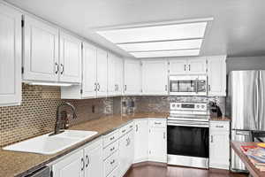 Kitchen with stainless steel appliances, white cabinetry, a sink, and tasteful backsplash