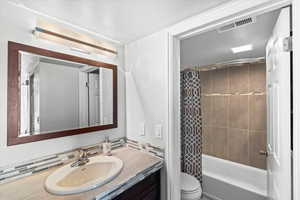 Bathroom with toilet, visible vents, shower / tub combo, and vanity