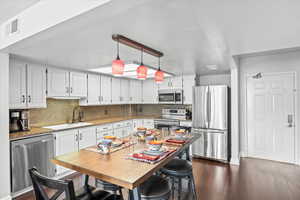 Kitchen with white cabinets, stainless steel appliances, decorative backsplash, and a sink