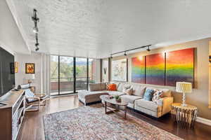 Living area with wood-type flooring, rail lighting, a textured ceiling, and a wall of windows