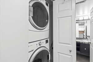 Washroom with a sink, tile patterned floors, stacked washer / drying machine, and laundry area