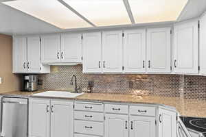 Kitchen with light countertops, decorative backsplash, a sink, and dishwasher