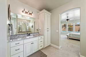 Bathroom featuring baseboards, connected bathroom, ceiling fan with notable chandelier, and vanity