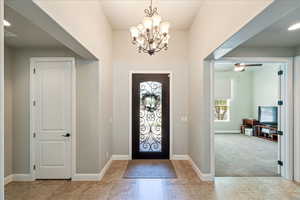 Carpeted entrance foyer with baseboards, ceiling fan with notable chandelier, and tile patterned floors