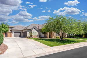 View of front of house with an attached garage, a front lawn, stone siding, stucco siding, and concrete driveway