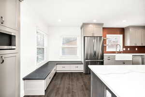Kitchen with dark wood-style flooring, stainless steel appliances, light stone countertops, and gray cabinets