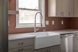 Kitchen featuring a sink, stainless steel dishwasher, gray cabinetry, and light stone countertops