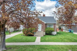View of front of property featuring a chimney, roof with shingles, brick siding, fence, and a front lawn