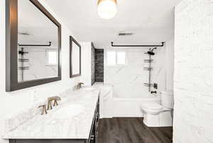 Full bath with a sink, double vanity, toilet, wood finished floors, and visible vents