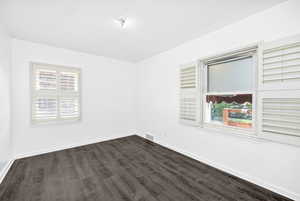 Empty room featuring dark wood-style flooring, baseboards, and a healthy amount of sunlight