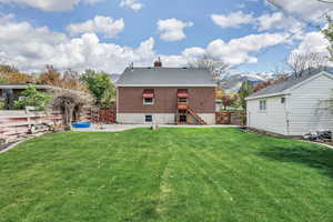 Rear view of house featuring a fenced backyard, a chimney, a yard, and brick siding