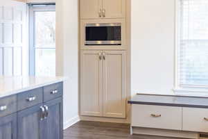 Kitchen with stainless steel microwave, visible vents, dark wood-style floors, and a wealth of natural light
