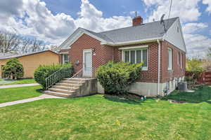 View of front facade with a shingled roof, a front lawn, brick siding, a chimney, and central air condition unit