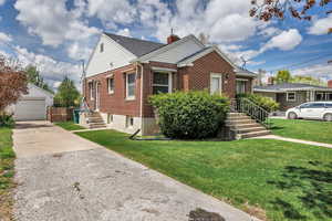 Bungalow-style house with a chimney, a front yard, brick siding, an outdoor structure, and concrete driveway
