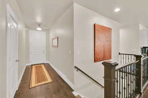 Corridor featuring baseboards, visible vents, dark wood finished floors, and an upstairs landing