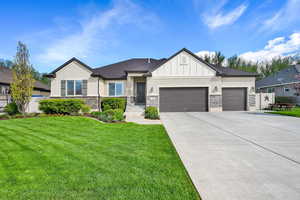 View of front of home with a garage, a front lawn, concrete driveway, stone siding, and stucco siding