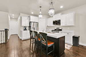 Kitchen with a breakfast bar area, appliances with stainless steel finishes, a sink, baseboards, and dark wood-type flooring