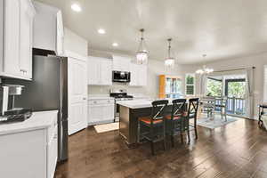 Kitchen with a breakfast bar, white cabinets, a sink, dark wood finished floors, and appliances with stainless steel finishes