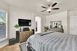 Bedroom featuring arched walkways, ceiling fan, and light carpet