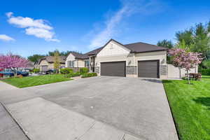 View of front of property with board and batten siding, driveway, a front yard, an attached garage, and stone siding