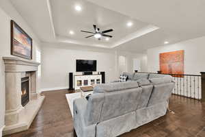 Living room featuring dark wood-type flooring, a ceiling fan, a tray ceiling, and recessed lighting
