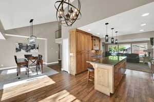 Kitchen with a notable chandelier, high vaulted ceiling, dark wood-type flooring, a kitchen island, and glass insert cabinets