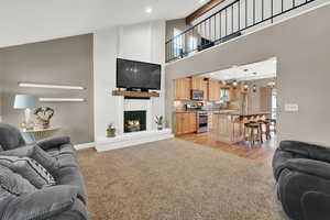 Living area featuring light colored carpet, light wood-style floors, a fireplace, high vaulted ceiling, and recessed lighting