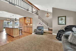 Living room with lofted ceiling, baseboards, stairway, light colored carpet, and a chandelier