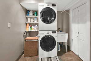 Clothes washing area featuring laundry area, baseboards, and stacked washer and clothes dryer