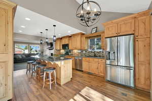 Kitchen featuring decorative backsplash, a kitchen bar, wood finished floors, an inviting chandelier, and stainless steel appliances