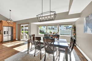 Dining space with baseboards, lofted ceiling, wood finished floors, and a notable chandelier